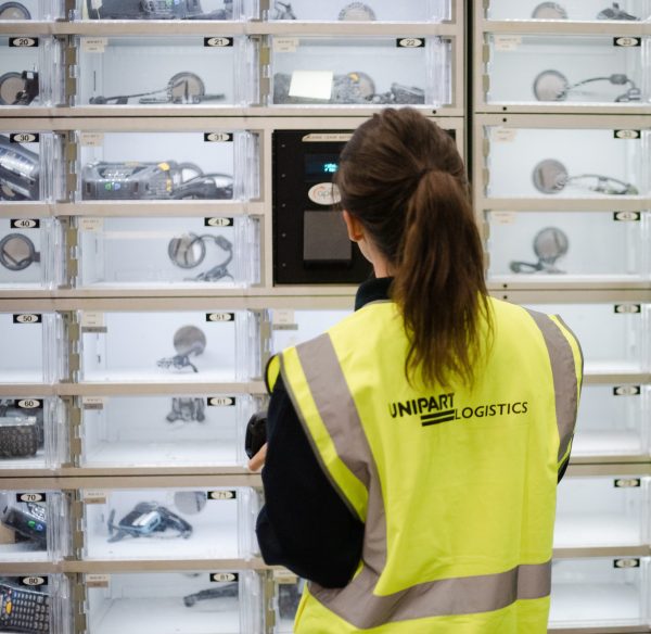 A woman in a Unipart Logistics safety tabard in front of lockers containing digital devices