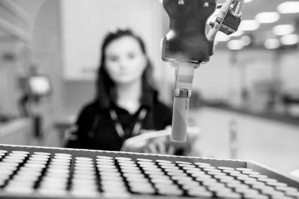 Black and white photograph of a woman moving a battery cell remotely using a robot in the Hyperbat facility