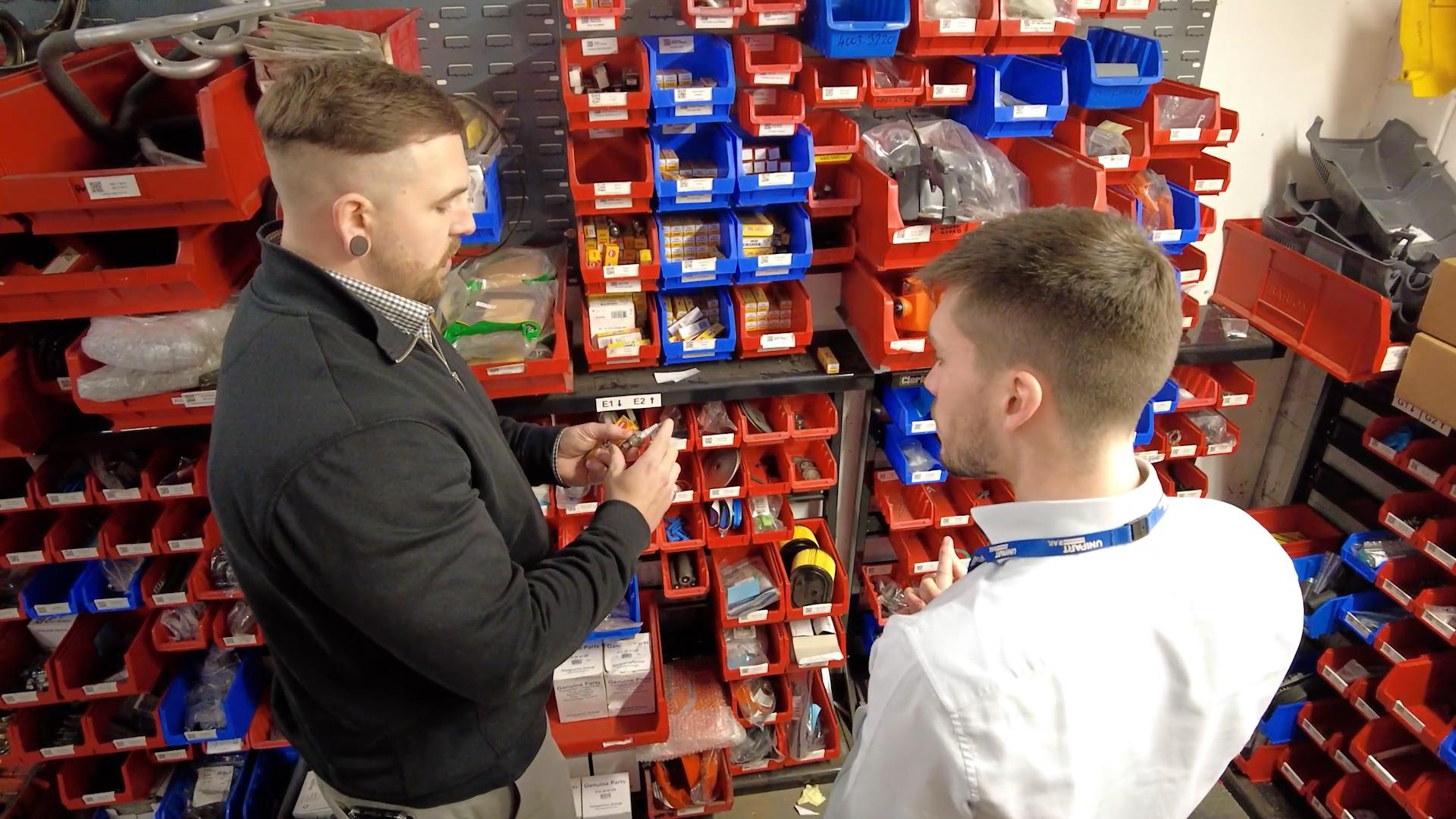 Two Unipart colleagues stood in front of lots of red and blue boxes of components.