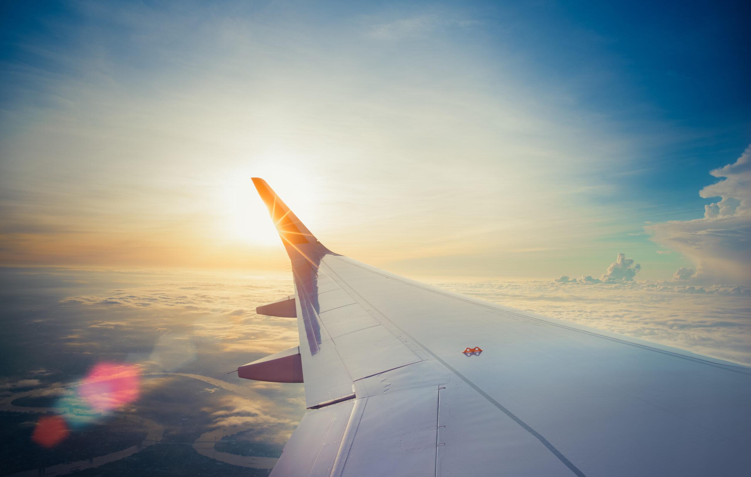 Wing of airplane flying above the clouds in the sunset sky background. View form the window plane through.