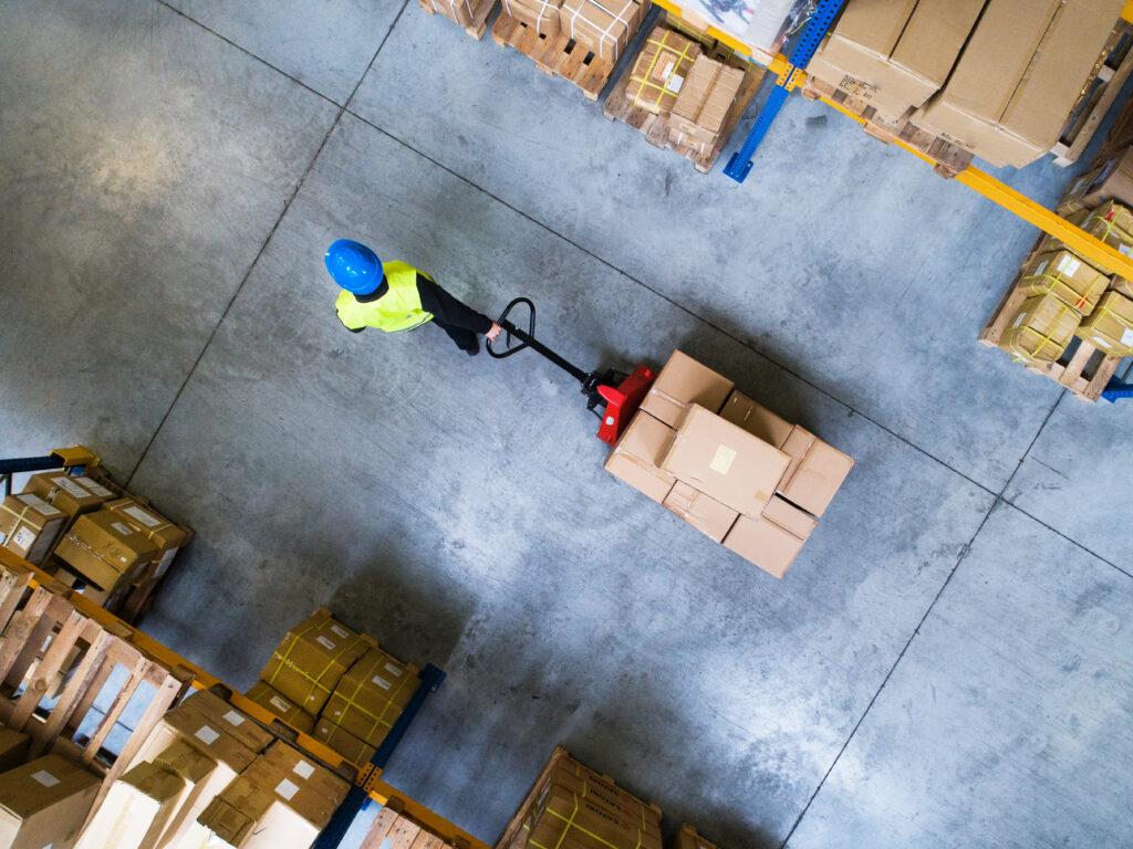 A warehouse worker pulling a pallet truck with boxes.