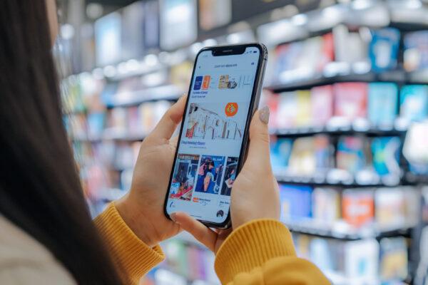 Woman in a shop holding mobile phone with online retail shop app open.