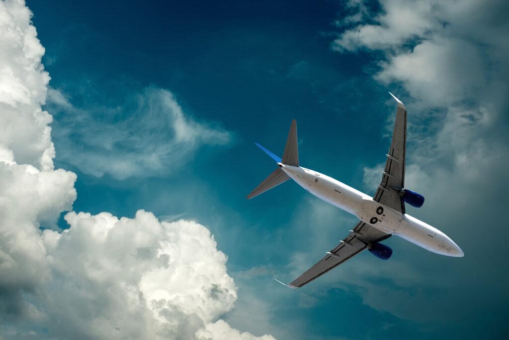 Airplane flying under sky with clouds