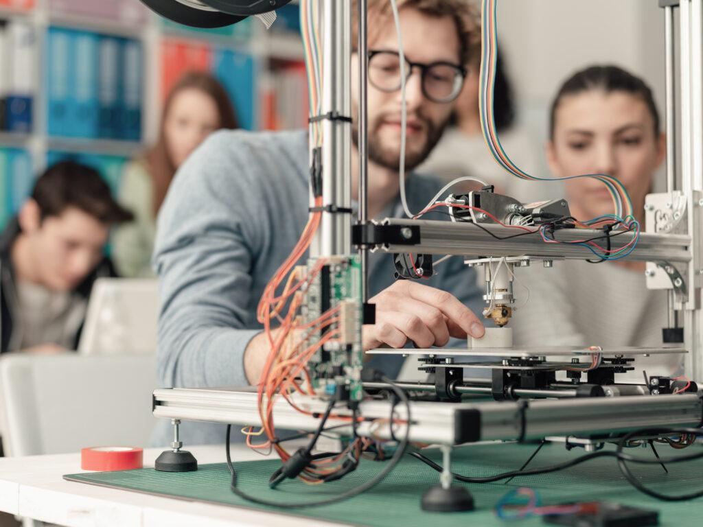 Male and female engineering students using a 3D printer in the lab, technology and learning concept