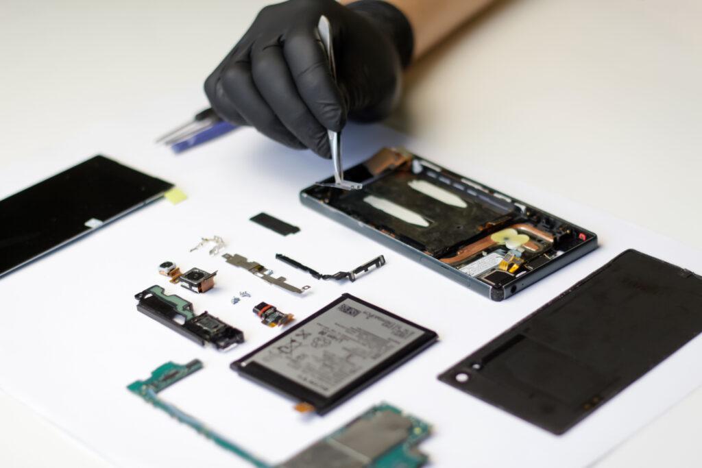 Professional repair of a disassembled smartphone, master with tweezers and gloves working on broken parts.