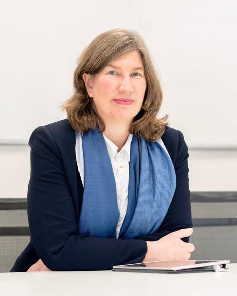 Catherine McDermott leaning on a deck wearing a navy suit jacket, white shirt and light blue scraf.