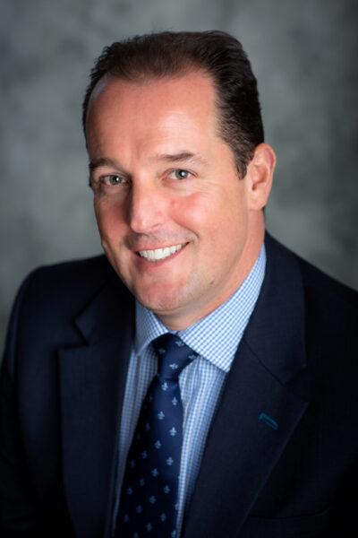 Headshot of Mark Johnstone in dark blue suit and light blue checked shirt.