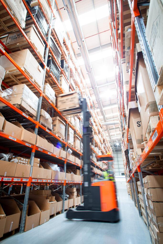 Red forklift moving in warehouse between racking.