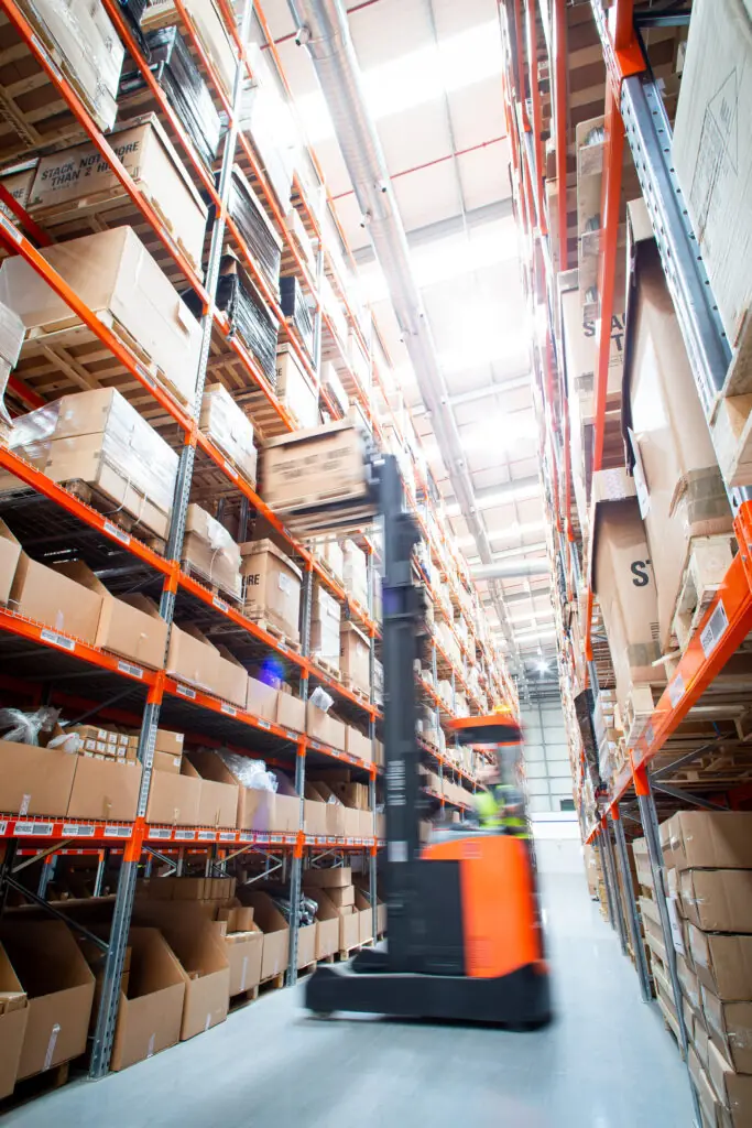Red forklift moving in warehouse between racking.