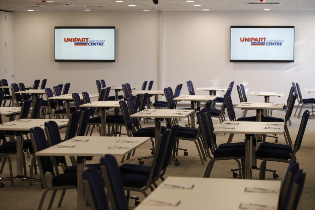 Unipart conference centre with tables set up and two screens in the background.