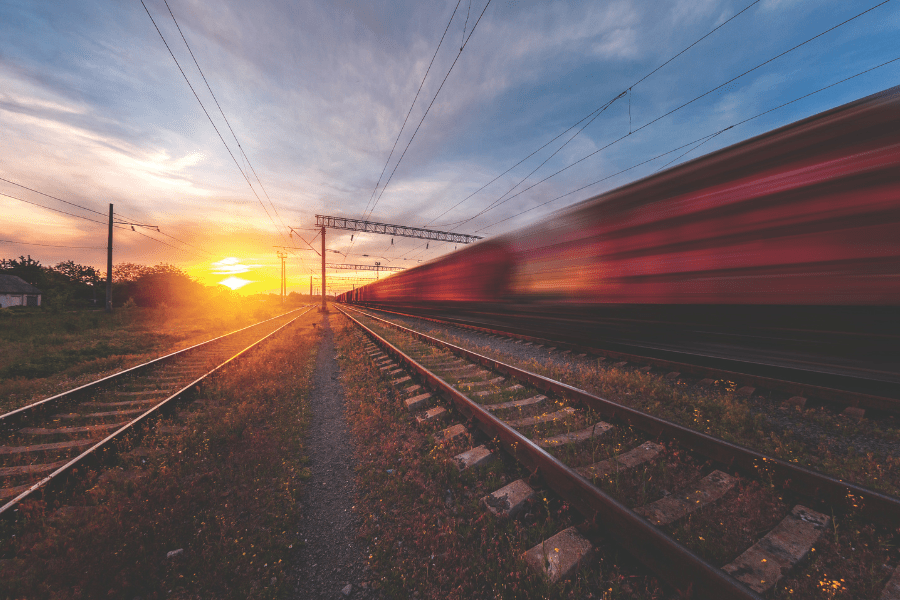 Long exposure of a train moving on tracks with the sun setting in the background.